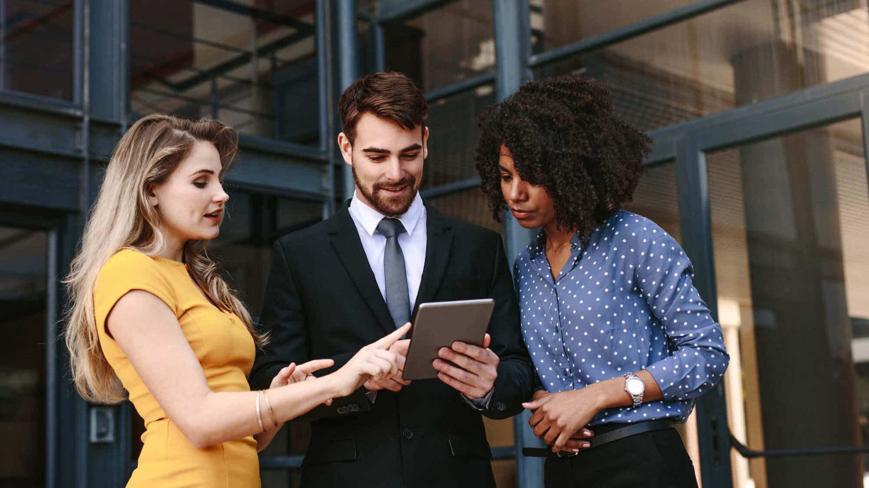 Three people review information on a tablet: Explore the certificate in business at Regent University.