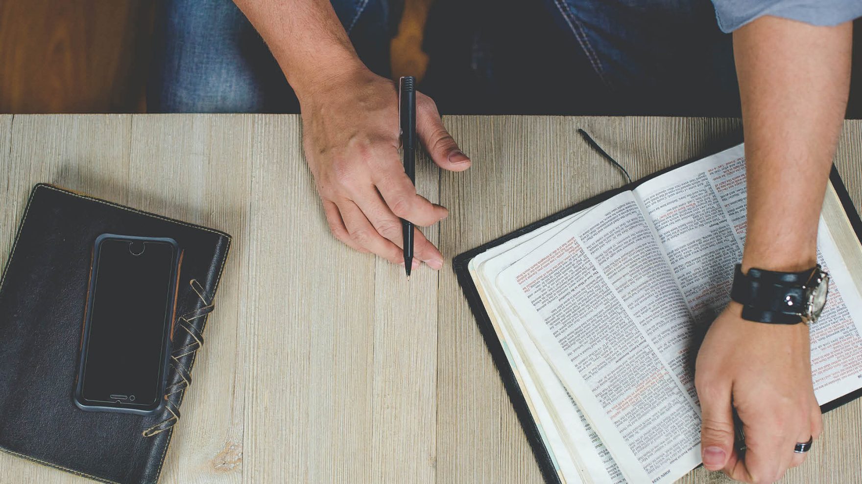 Top view of hands of a Regent University student studying in the Certificate in Christian Ministry program opening a Bible and holding a pen to make notes