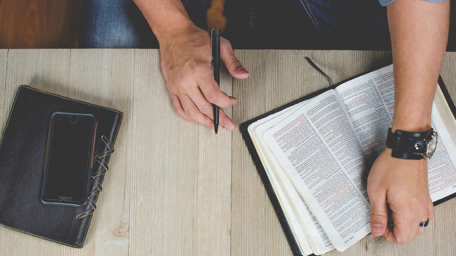 Top view of hands of a Regent University student studying in the Undergraduate Certificate of Biblical Studies program opening a Bible and holding a pen to make notes