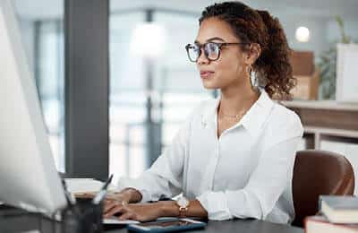 A woman working on  her computer: Access resume building assistance at Regent University's career services.