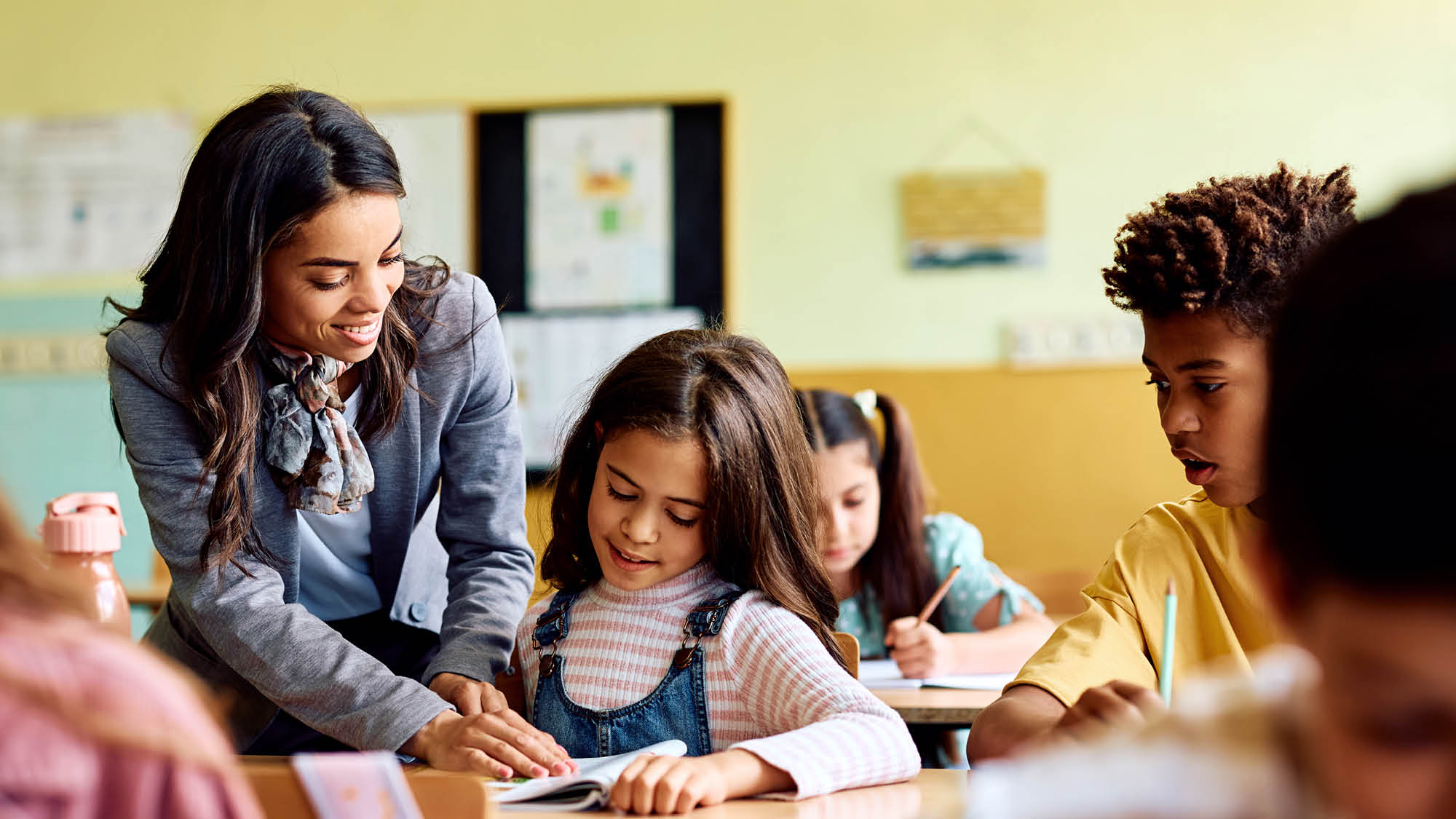 A teacher from Regent University's School of Education Career Switcher program pointing at a workbook on a students' desk in a classroom.