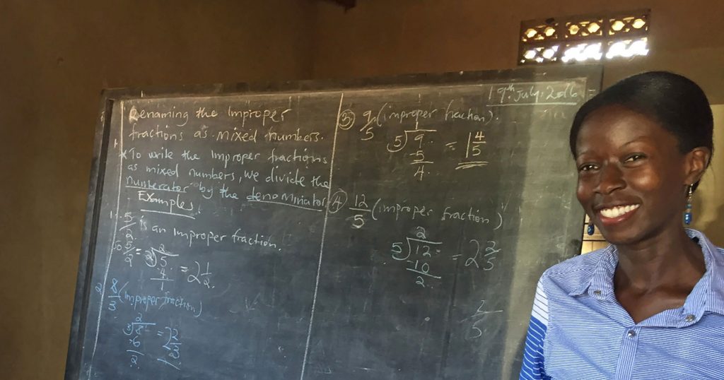 Regent University online student Prudence Nakaweesa smiles next to classwork on a chalkboard.